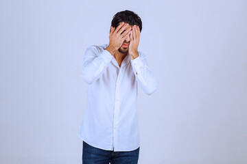 Man in white shirt coverin his face, feels sad and has headache