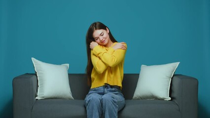Smiling young girl hugs herself feeling self love and care, sitting on sofa. Body positive, acceptance, good self esteem