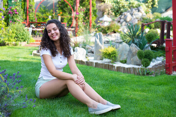 Young smiling woman sitting on the green grass of her garden on a beautiful summer day