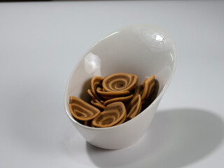Shell-liked cookies, called Spiral Cookies, Helix Crackers, Ear Cookies or Pig Searcrackers, in a bevel white ceramic plate dish as a photo
