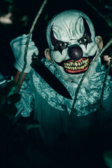 evil clown with a knife in the woods at night