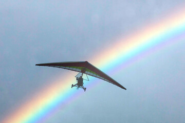 Deltaplano in volo sotto un cielo con arcobaleno