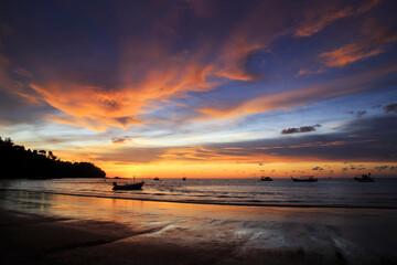 Dramatic clouds and mirror reflections on water.Twilight sky and cloud with orange sun nature background.Beautiful sunset on the beach with mountain and sky clouds.Wooden fishing boat on the sea.