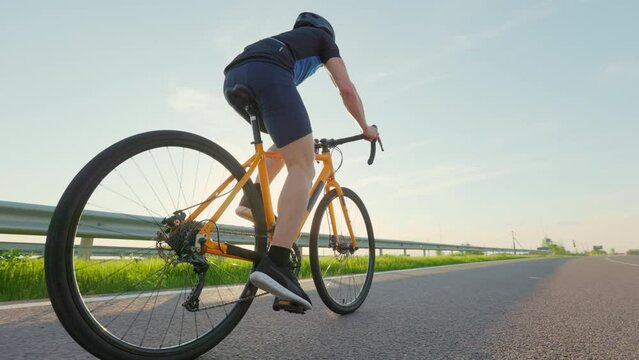 Professional racing biker in sportswear, helmet and sunglasses riding along asphalt road among beautiful green nature. Concept of sport and training.