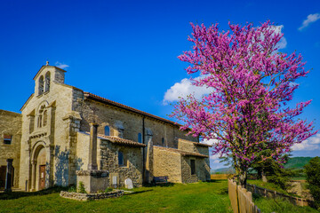 Fototapeta na wymiar View on the romanesque facade of the Saint Agnes church in Saint Jean de Galaure (Ardeche, France) with a blossoming tree with pink flowers