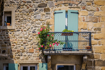 Fototapeta na wymiar Facade of an old stone house, with flowery balcony and closed light shutters in the South of France (Champagne, Ardeche)