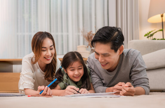 Happy Asian family father, mother, and daughter relaxing by playing and painting together on carpet in the living room at home.