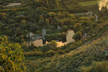 High view of the castle and lake of the garden of Ninfa in Cisterna di Latina, Norma, near Rome Italy at sunset. Natural monument in Italy The garden in English style - obrazy, fototapety, plakaty