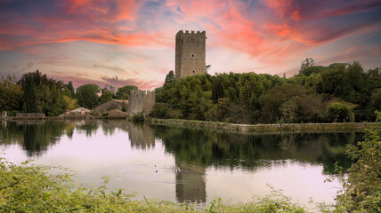 The castle and lake of the garden of Ninfa in Cisterna di Latina, Norma, near Rome Italy at sunset. Natural monument in Italy. The garden in English style. Romantic medieval knight view. - obrazy, fototapety, plakaty