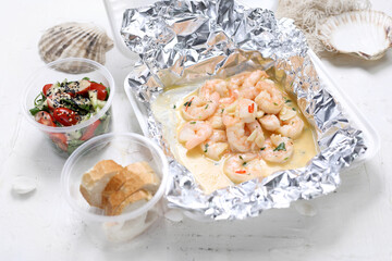 Shrimps in wine, butter and garlic, sprinkled with parsley. King prawns in a take-away carton box, on white background.
