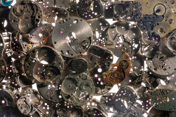 Top view of heap of metal internal parts of an old clock on a white light background. Silver...