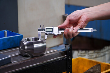 Hands of an engineer measures a metal part with a digital vernier caliper. Quality control of part...