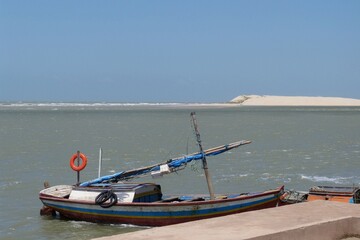 Obraz premium Small wooden sailboat moored at a pier in a bay and in the background a sand dune in São Luís, Maranhão, Brazil.