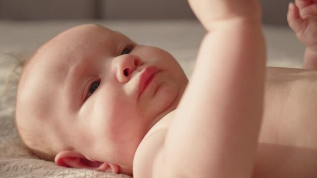 Cute tiny baby with bare belly looks up, slow motion.  Beautiful newborn baby., closeup face. Active newborn boy lies on the bed and moves his arms. Low angle view of a chubby male baby..