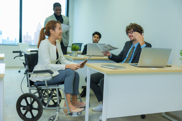 Asian woman who use the wheelchair working in office with diversity of colleague.