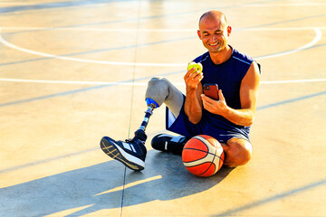 sporty handicapped man in sportswear and with artificial leg basketball player at sunset eating an...