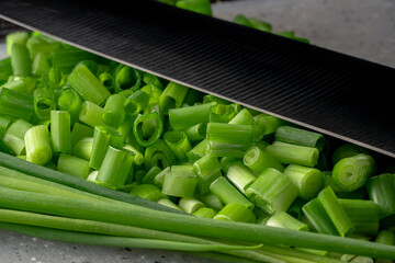 Chopped pieces and of green onion stalks. Slices and stems of fresh green scallion next to the knife blade. Chopped shallots or chive, seasonal greenery, seasoning for salad. Macro shot.