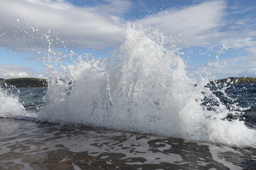 A rising wave hitting the coastline from the open sea.