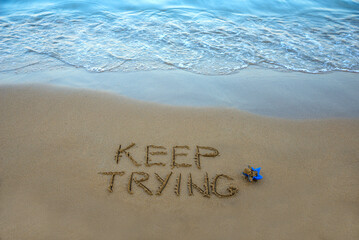 Keep trying  written in the sand on the beach with the sea washing up the shore