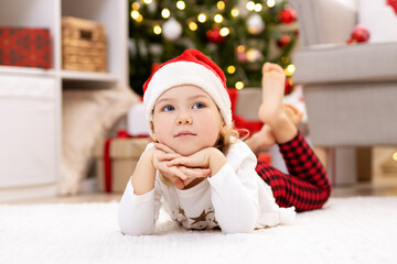 Obraz na płótnie Canvas Dreaming little girl lying on carpet near Christmas tree