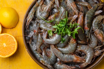 Plato de gambas frescos preparados para cocinar con limon y naranja en bandeja amarilla