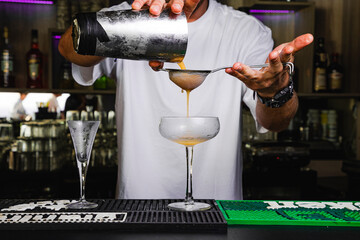 Barman preparando cóctel naranja de guayaba con colador en copa de cristal fría