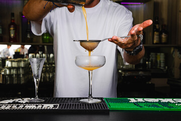 Fototapeta na wymiar Barman preparando cóctel naranja de guayaba con colador en copa de cristal fría