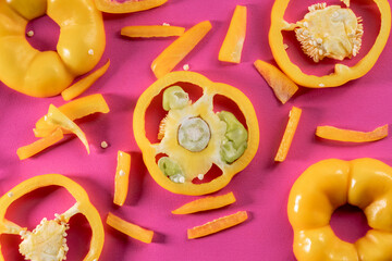 Sliced rings of yellow sweet pepper on a pink background. Top view of sweet pepper pieces with juicy pulp and seeds. Fresh ripe sliced vegetables close up. Fresh raw ingredients for salad.