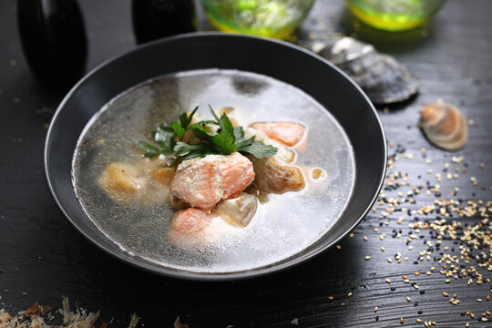 Fish soup with salmon. Black bowl with fish broth soup, on a black table, top view.