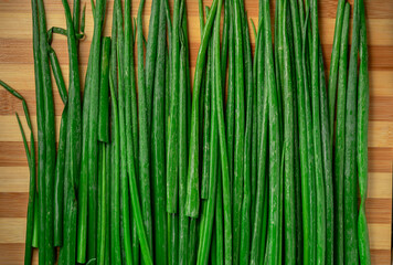 Stems of fresh green onions with drops of water on a striped wooden kitchen board. Juicy wet cut stalks of green onions. Greenery, seasoning for cooking fresh healthy salad. Close up.