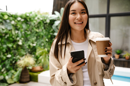 Young asian woman using cellphone while drinking coffee