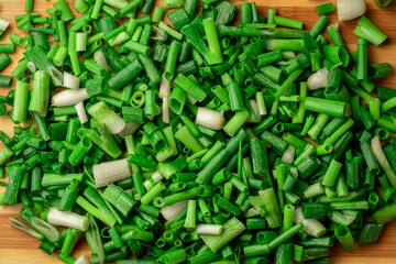 Chopped pieces of fresh green onions on striped wooden kitchen board. Juicy chopped green scallion or chives slices and white stems. Greenery, seasoning for cooking fresh healthy salad. Close up.