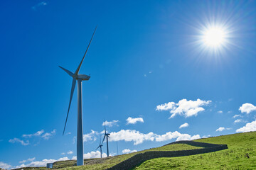 Three wind turbines, shot in landscape against a blue sky  with a sun star and dry stone wall
