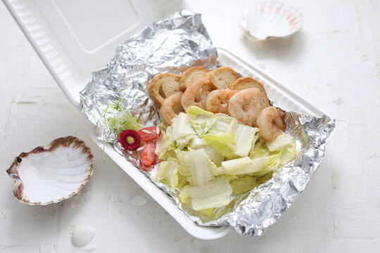 King prawn salad. Shrimp salad with iceberg lettuce in a take-away carton box, on a white background, top view.