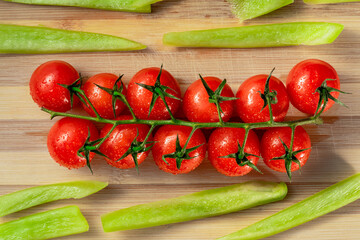 A bunch of ripe red cherry tomatoes and chopped pieces of green sweet pepper on a striped wooden board. Top view of tomatoes and sweet peppers wet from moisture drops. Fresh vegetables. Close up.