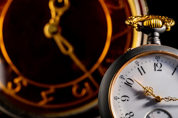 Silver antique pocket watch with gold hands and vintage table clock in blurry background. An old...