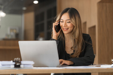 Using mobile, cheerful young asian business woman working at working place.