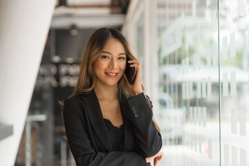 Fototapeta premium Using mobile, cheerful young asian business woman working at working place.