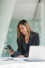 Obraz premium Using mobile, cheerful young asian business woman working at working place.