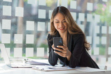 Obraz premium Using mobile, cheerful young asian business woman working at working place.