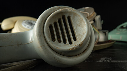 Tube from an white old rotary landline phone on black background. Macro shot of dirty plastic telephone receiver with holes. Removed phone handset on dark wooden table. Vintage shabby phone receiver.