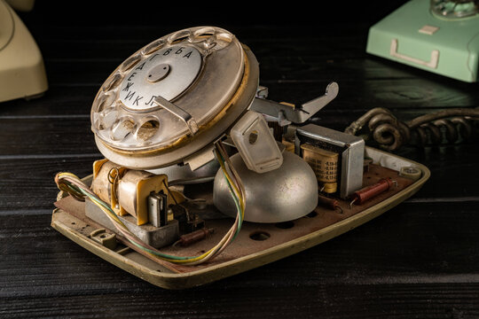 Old disassembled rotary telephone on a black wooden table. Internal parts, green, yellow and white twisted wires in the dust. Close up of vintage broken rotary dialer with round holes and numbers.
