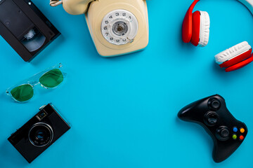 Camera, sunglasses, VHS videotape. Rotary phone, red white headphones, video game joystick on blue background with copy space. Retro, vintage, history, nostalgia concept. Top view. © kinomaster