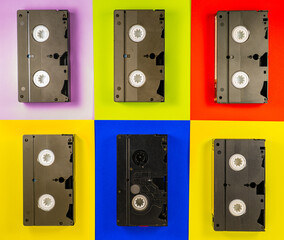 Obraz premium Black vintage VHS videotapes on red, blue, yellow, pink background. Plastic retro video cassettes with analog magnetic tape from 90s. Old technology for tape recording and watching movies. Top view.