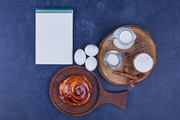 Pastry bun with ingredients on a wooden platter with a receipt book aside
