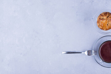 A cupcake in a glass cup served with hot chocolate on the right side of the table