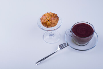 A cupcake in a glass cup served with hot chocolate on blue background