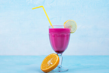Pink juice in a glass cup with yellow pipes on blue background