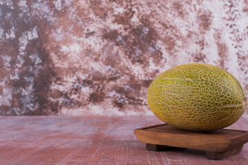 Yellow melon on a wooden platter isolated on pink background