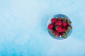 Red strawberries in a glass cup on blue background on the right